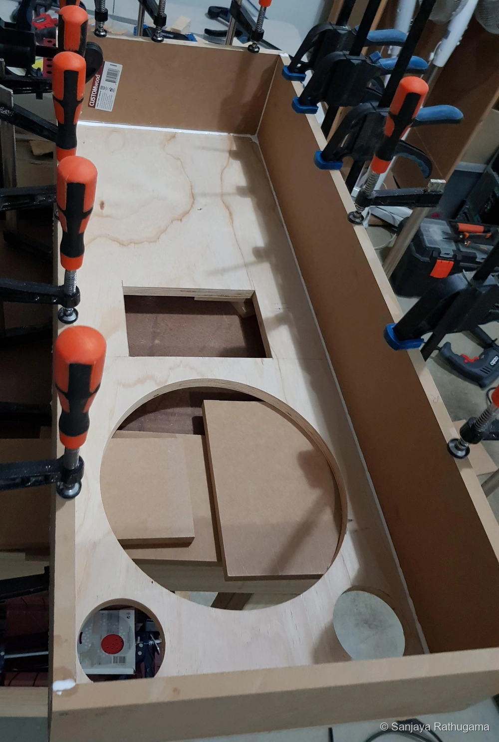 View into the clamped shallow LCR enclosure, showing the plywood baffle with horn, woofer and dual-port cut-outs