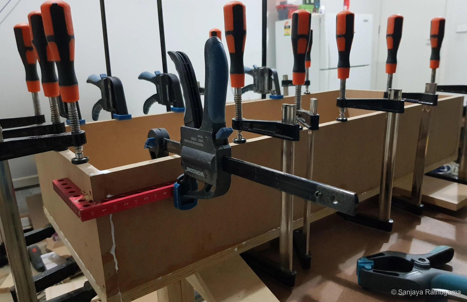 Close-up of the shallow cabinet corner held with bar clamps and a red right-angle clamping aid