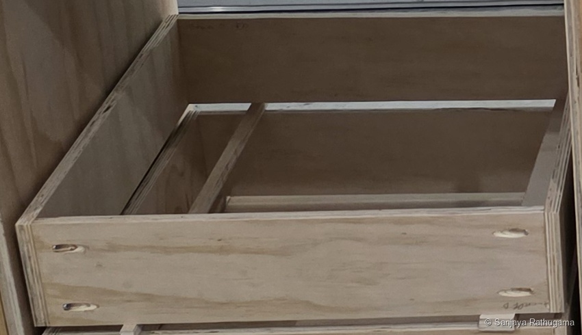 Close-up of an open plywood drawer box, showing two pocket holes near each end of its front panel and the side panels meeting it at the corners