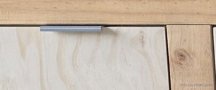 Close-up of a custom 3D-printed handle fitted near the upper edge of a plywood drawer front